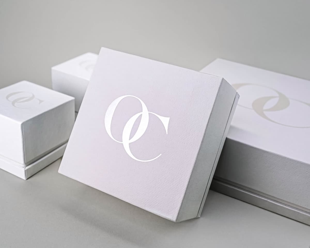 OC Tanner — white textured rigid jewelry boxes with silver foil monogram across multiple sizes